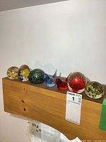 View of all seven items, five glass paperweights and two glass bird figurines arranged on a wooden surface.