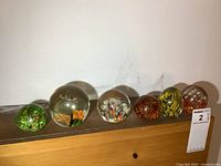View of all six glass paperweights lined up on brown surface against white wall.
