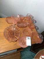 Full assortment of pink depression glass including bowls, dishes, creamers and sugar dish on a wooden surface.