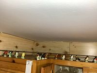 Wide view of all 14 small porcelain bird figurines lined up on a wooden shelf under lighting.
