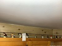 Wide view of 10 small porcelain bird figurines lined up on a wooden shelf beneath a brass rod.