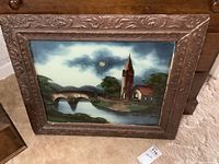 Full view of the reverse glass painting in its ornate wooden frame against a beige carpet and furniture background.