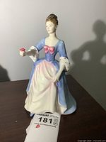 Porcelain Royal Doulton figurine 'Valerie' approximately 8 inches tall, dressed in blue and pink gown holding a rose, displayed on dark surface.