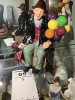 Front view of the Royal Doulton Balloon Man figurine holding colorful balloons, sitting on a wooden crate with a visible Royal Doulton tag.