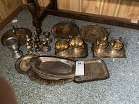 Wide shot showing all silver plate items arranged on carpet. Includes trays, candle holders, cream and sugar sets, and shakers.