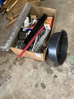 Box with assorted small engine parts including oil change pan, mower blades, oil filters, carburetors, and tools