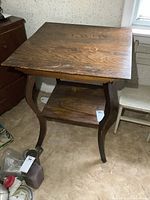 Front view showing table top, curved legs, and lower shelf on carpeted floor near wall and chair.