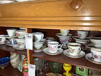Photo showing two shelves filled with vintage teacups and matching saucers with floral patterns, various colors, and gold trim.