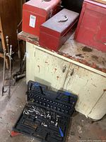 Two metal toolboxes (red and silver) on cabinet along with black plastic socket case showing worn surfaces and carry handles