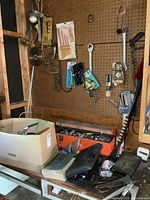 Photo of toolbox and box of assorted tools on shelf below pegboard with various hand tools hung on pegboard