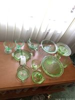 Overview of nine green glass pieces arranged on wood table beneath window light