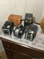 Four vintage Kodak Brownie cameras on lace cloth, wooden and stone background.