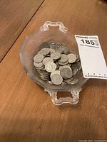 A transparent bowl filled with numerous circulated Canadian 5 cent coins from 1951 and other years, placed on a wooden surface.