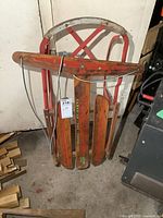 Front view of vintage child's sleigh with metal frame and wooden slats, red paint with signs of rust and wear