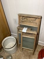 Overall view of three wooden washboards and enamel pot on beige carpet against white wall.