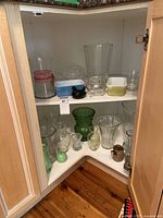Corner cabinet with varied glassware and decorative vases, including green vase, glass chicken, small vases, and cups.