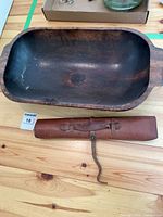 Wooden dough bowl showing the interior with a dark patina and the brown leather roll placed beneath it.
