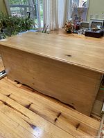 Front and side view of the wooden chest showing natural wood with a smooth top and paneled sides with finger joint corners.