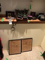 Wide shot showing rotary phone, shaving kit box, vintage camera, binoculars, trophies, keys and framed newspapers beneath shelf