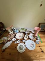 Full lot overview showing diverse assortment of plates, bowls, vases, and teacup sets arranged on wooden table