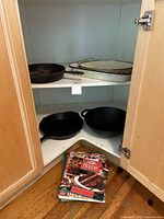 Kitchen cabinet corner shelf with cast iron and enamel cookware and a stack of cookbooks on floor
