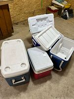 Four coolers in a garage setting, various colors and sizes.