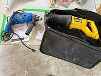 Mastercraft hammer drill and Dewalt reciprocating saw placed side by side, power cords visible, on a concrete floor.