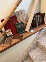 Photo of wooden staircase ledge holding a collection of worn books, folded map, rolled poster, a red book titled '165 Views of London', a green book titled 'English Prose', a Plane Packet tin, and a small brown leather wallet.