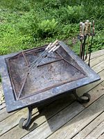 Photo showing overall view of the fire pit on a wooden deck with fire tools placed on top.