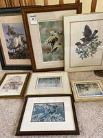 Overall view of eight framed artwork prints arranged on a beige carpet. Subjects include various bird images and architectural sketches.