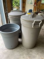 Three garbage containers: two beige Rubbermaid with lids and wheels, one smaller gray container without lid.