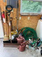Full view of the gardening tools lot showing shovels, brooms, rake, garden hoses, watering cans, and miscellaneous tools in plastic tubs.