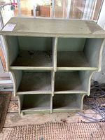 Front view of green wooden shelf with six compartments showing dirt and wear.
