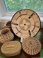 Image showing 5 handwoven baskets and bowls arranged on wooden table in front of window, displaying varied sizes and patterns.