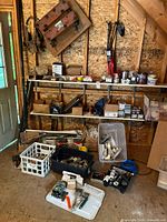 Photo of garage shelves and floor with various handyman supplies including hardware, painting tools, tool belt, and boxes.