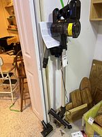 Full view of the Hoover Emerge Pet Cordless vacuum standing upright with metal wand, hose and floor nozzle attached, user manual inserted behind main unit.