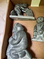 Three soapstone Inuit carvings in box: kneeling scraping figure, seated figure, standing figure