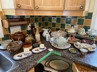 Wide view of kitchen countertop displaying the assortment of kitchenware and serving dishes including teapots, bowls, salt and pepper shakers, and decorative items.