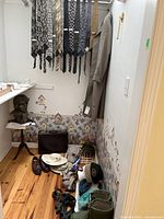 Room corner with men's ties hanging, beige coat, dress shoes on floor, hats and suspenders visible