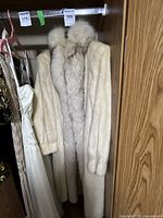 Full view of vintage ranch mink fur coat hanging in closet showing cream color and large collar.
