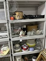 Shelf displaying kitchenware items including metal baskets, tins, hot plate, teapot, glass bowls and espresso cups.