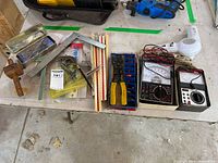 Lot overview showing multiple hand tools including wire stripper, multimeters, pliers, carpenter square and wooden mallet.