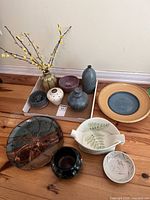 Wide view of assorted pottery including vases, bowls, and decorative ceramic pieces arranged on wooden floor.