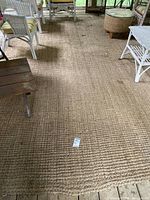 Full view of natural brown woven jute rug on floor under wicker furniture showing general wear and dirt.