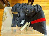 Uniform jacket displayed with sergeant chevron insignia patches and pants folded beside it. Shows brass buttons and chevrons on sleeve.