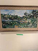 Full view of the oil painting showing scene of bay with water lilies and houses surrounded by trees and foliage in carved wood frame.