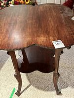 Front angle view of the ornate wood cloverleaf accent table showing the tabletop and legs.