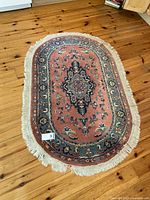 Full view of oval area rug with coral and blue colors on wooden floor showing overall condition and shape