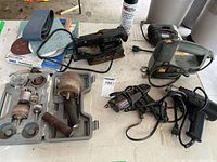 Overview of power tools set on table including sander, jigsaw, heat & strip tool, sanding belts, polishing discs and attachments.