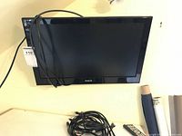 Front view of black RCA 21 inch flat screen TV mounted on wall with power cable and remote shown beneath.